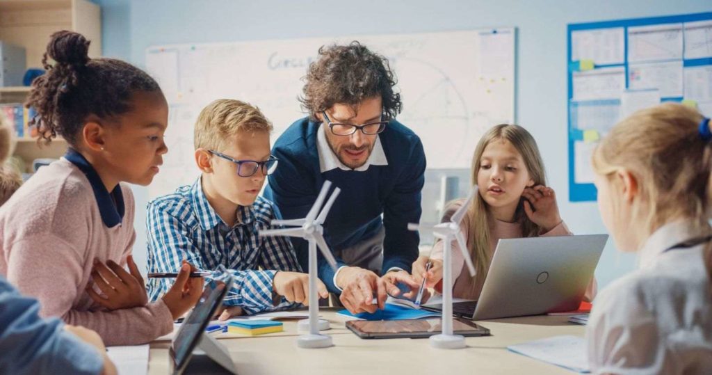 A teacher showing some students something on a laptop.